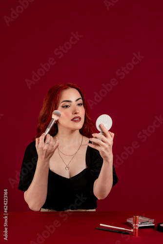 Woman applying makeup on her face against a colored isolated background.