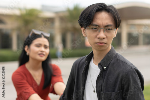 A young asian woman desperately holds on to her upset boyfriend, imploring him not to leave her. A breakup scenario initiated by the man.