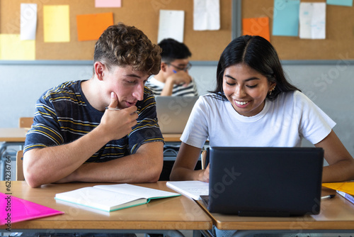 Canvas Print Caucasian teen boy and native american teenage female high school students in class working together using laptop