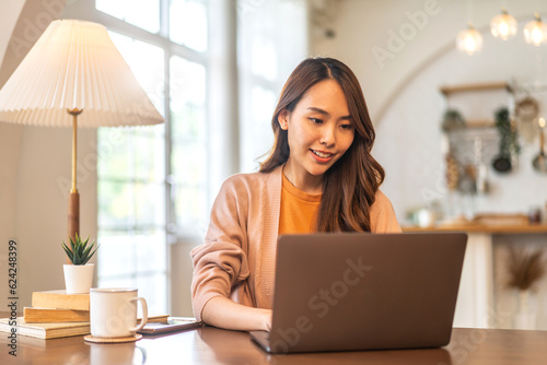 Young smiling happy beautiful asian woman relaxing using laptop computer in the bedroom at home.Young creative girl working and typing on keyboard.work from home concept