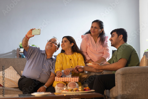 Senior man taking selfie of his family while sitting together at home on Raksha Bandhan