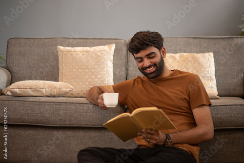 Smiling young man drinking tea while relaxing on sofa in living room