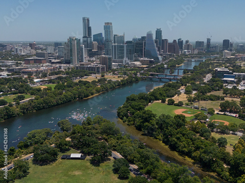The skyscrapers of Austin, Texas are shown with the Colorado River / Lady Bird Lake visible in the foreground during a summer day from an elevated view.