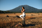 A couple of young people, a man and a woman, of European appearance, are engaged in acroyoga in nature, against the backdrop of Agung volcano, Bali.