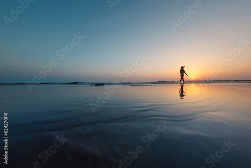 silhouette of a woman walking along the seashore. Spiritual Peace Meditation. A happy girl walks along the seashore against the backdrop of sunset. © zhukovvvlad