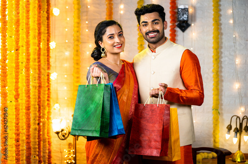 Happy young indian couple with shopping bags in hand looking camera - concept of festival offers, promotional sales and discount