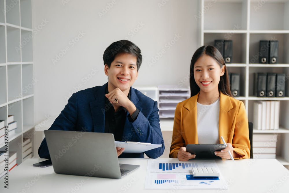Asian business colleague business presents and explains and using laptop and tablet. Teamwork, financial marketing team,   while sitting in modern office room..