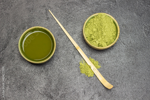 Bamboo measuring spoon on the table. Green matcha tea powder and matcha tea in green bowls.