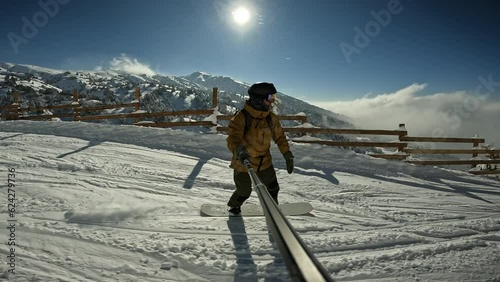 Male millennial cheerful snowboarder having fun snowboarding backcountry on sunny winter day in snowy mountains. Extreme freeride snowboarder riding on snowy track at fence that prevents falls  photo