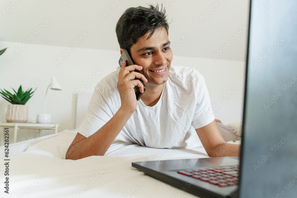 Smiling man lying on bed and talking on smart phone at home Smiling man lying on bed and talking on smart phone at home