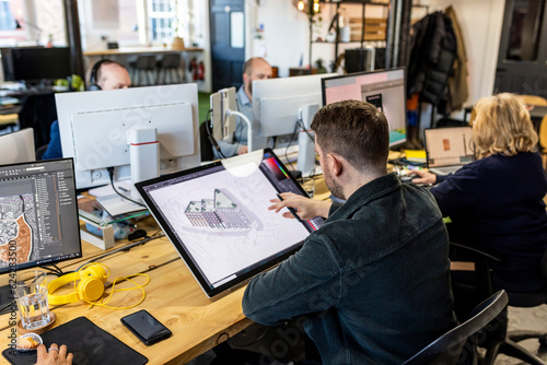 Architect working on graphics tablet with colleagues at desk in office photo