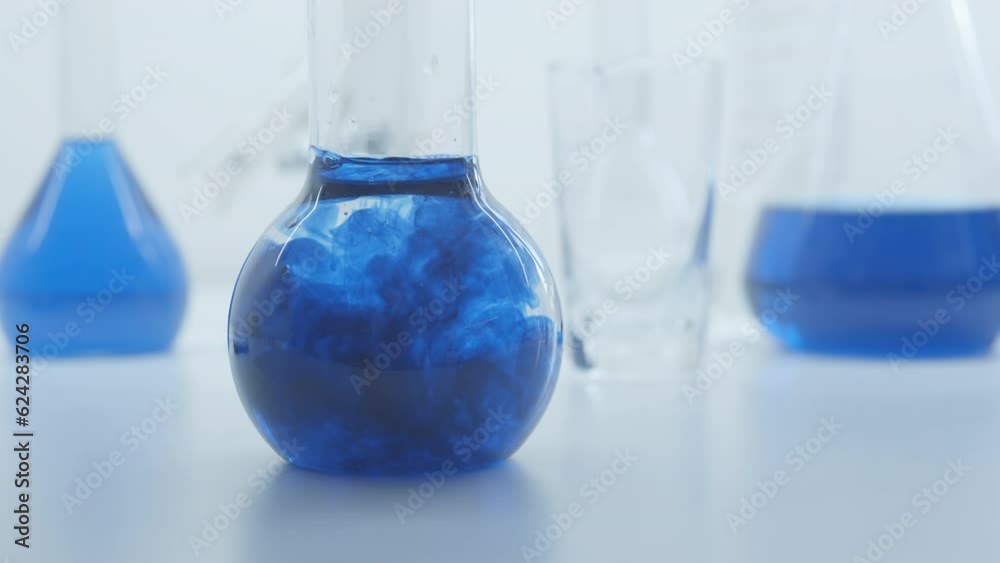 Blue liquid substance dissolve in a glass flask. Concept for advertising perfume and cosmetic products. Mixing blue ink with water in a large laboratory glass test tube. Blue liquid substance dissolve in a glass flask. Concept for advertising perfume and cosmetic products. Mixing blue ink with water in a large laboratory glass test tube.
