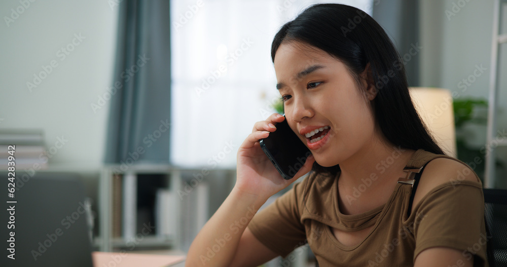 Young Asian woman working with a laptop on a desk while talking on phone