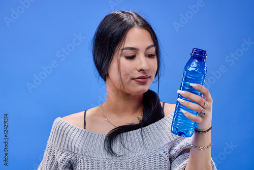 Portrait of a beautiful young brunette posing in the studio on a blue background with a bottle of water in her hand