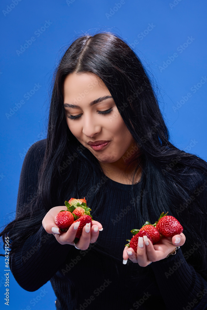 Portrait of a beautiful young brunette eating strawberries, isolated on a blue background Portrait of a beautiful young brunette eating strawberries, isolated on a blue background