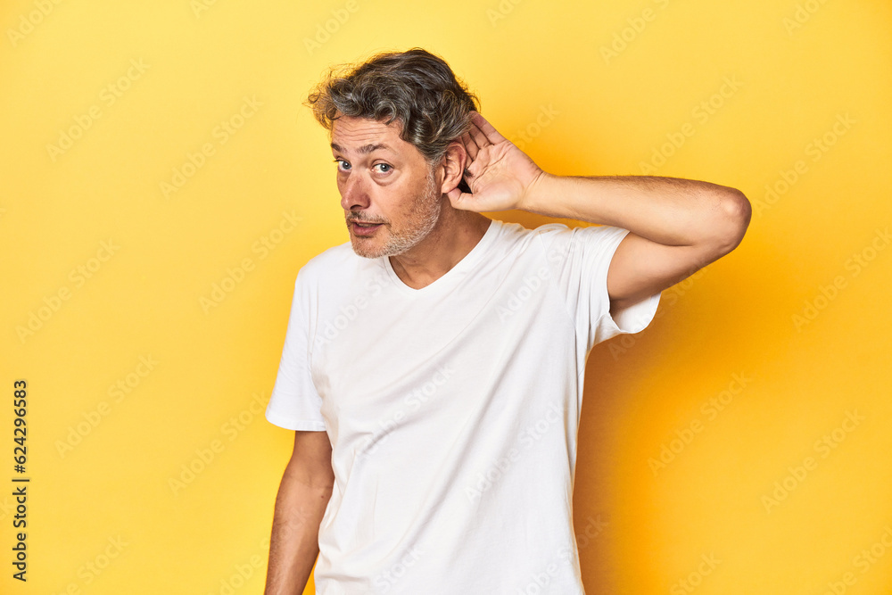 Middle-aged man posing on a yellow backdrop trying to listening a gossip. Middle-aged man posing on a yellow backdrop trying to listening a gossip.