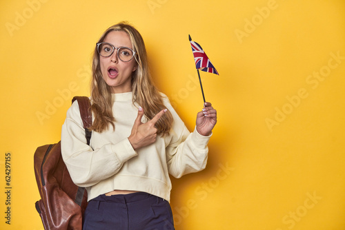 UK flag-waving student, Erasmus concept on yellow backdrop, pointing to the side