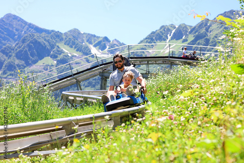 Fototapeta father and child having ride on summer toboggan called Rodelbahn rushing down the track