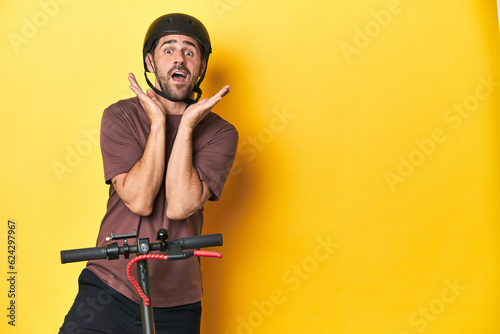 Man with electric scooter and helmet, yellow studio surprised and shocked.