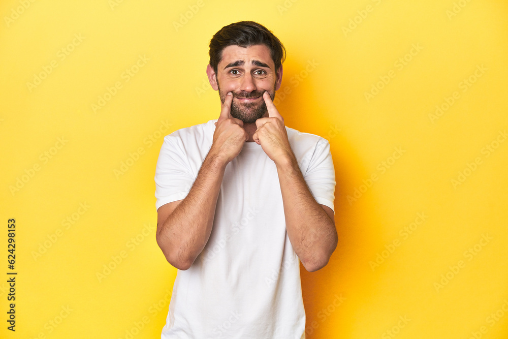 Caucasian man in white t-shirt on yellow studio background doubting between two options. Caucasian man in white t-shirt on yellow studio background doubting between two options.