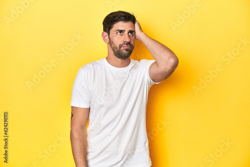 Caucasian man in white t-shirt on yellow studio background tired and very sleepy keeping hand on head.
