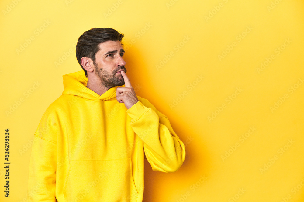 Man in yellow hoodie, monochrome studio backdrop looking sideways with doubtful and skeptical expression. Man in yellow hoodie, monochrome studio backdrop looking sideways with doubtful and skeptical expression.