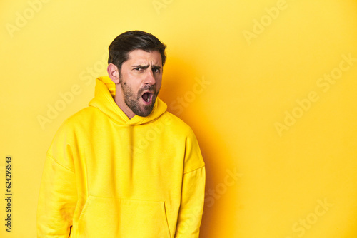 Man in yellow hoodie, monochrome studio backdrop shouting very angry, rage concept, frustrated.