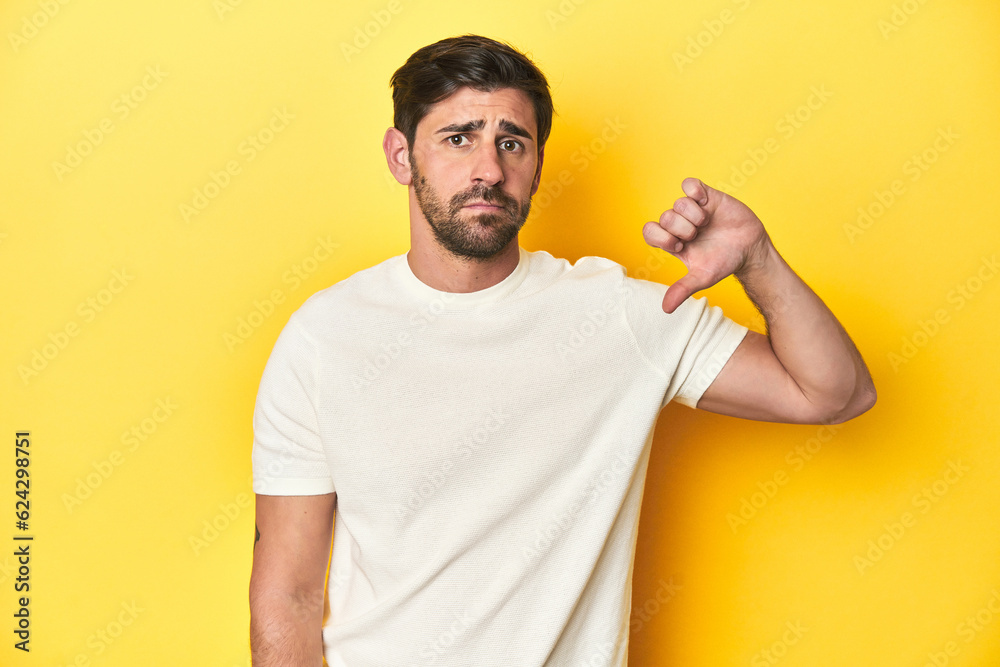 Caucasian man in white t-shirt on yellow studio background showing a dislike gesture, thumbs down. Disagreement concept. Caucasian man in white t-shirt on yellow studio background showing a dislike gesture, thumbs down. Disagreement concept.