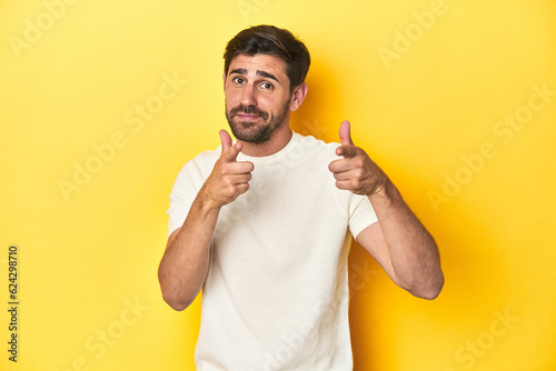 Caucasian man in white t-shirt on yellow studio background pointing to front with fingers.