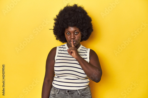 African-American woman with afro, studio yellow background keeping a secret or asking for silence. © Asier