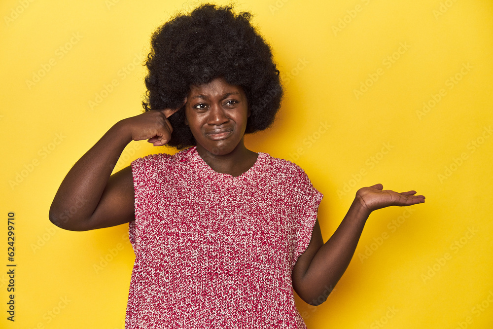 African-American woman with afro, studio yellow background holding and showing a product on hand. African-American woman with afro, studio yellow background holding and showing a product on hand.