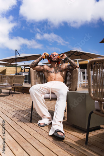 Chico joven tatuado y musculoso posando en terraza de chiringuito en vacaciones