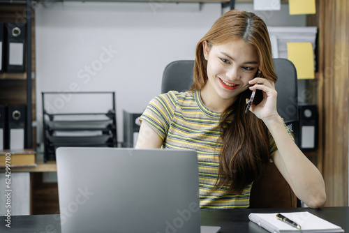 Consulent speaking to mobile cellphone at home office. women speak with remote clients using phone. Laptop on the desk. Home office smart working concept lifestyle. © NINENII