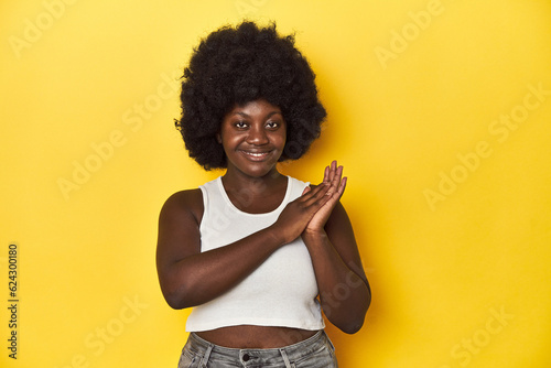 African-American woman with afro, studio yellow background feeling energetic and comfortable, rubbing hands confident.