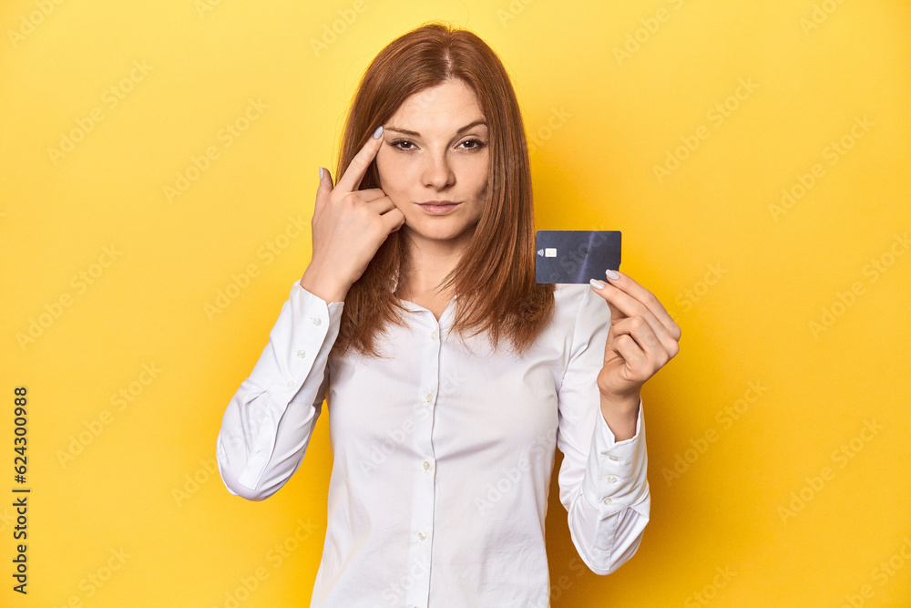 Redhead holding credit card, financial concept showing a disappointment gesture with forefinger. Redhead holding credit card, financial concept showing a disappointment gesture with forefinger.