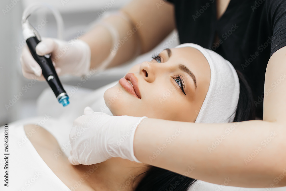 Professional dermatologist in medical gloves doing hydro peeling procedure for beautiful woman patient in cosmetology clinic. Close up facial treatment. Professional dermatologist in medical gloves doing hydro peeling procedure for beautiful woman patient in cosmetology clinic. Close up facial treatment.