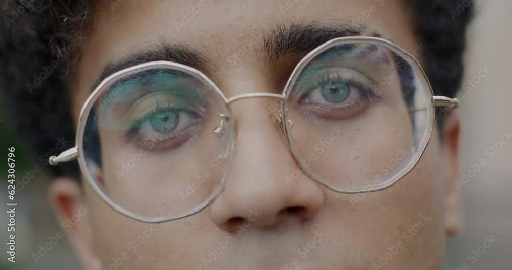Close-up slow motion portrait of Middle Eastern man's face with eyeglasses looking at camera on outdoor background. Eyesight and youth concept. Close-up slow motion portrait of Middle Eastern man's face with eyeglasses looking at camera on outdoor background. Eyesight and youth concept.