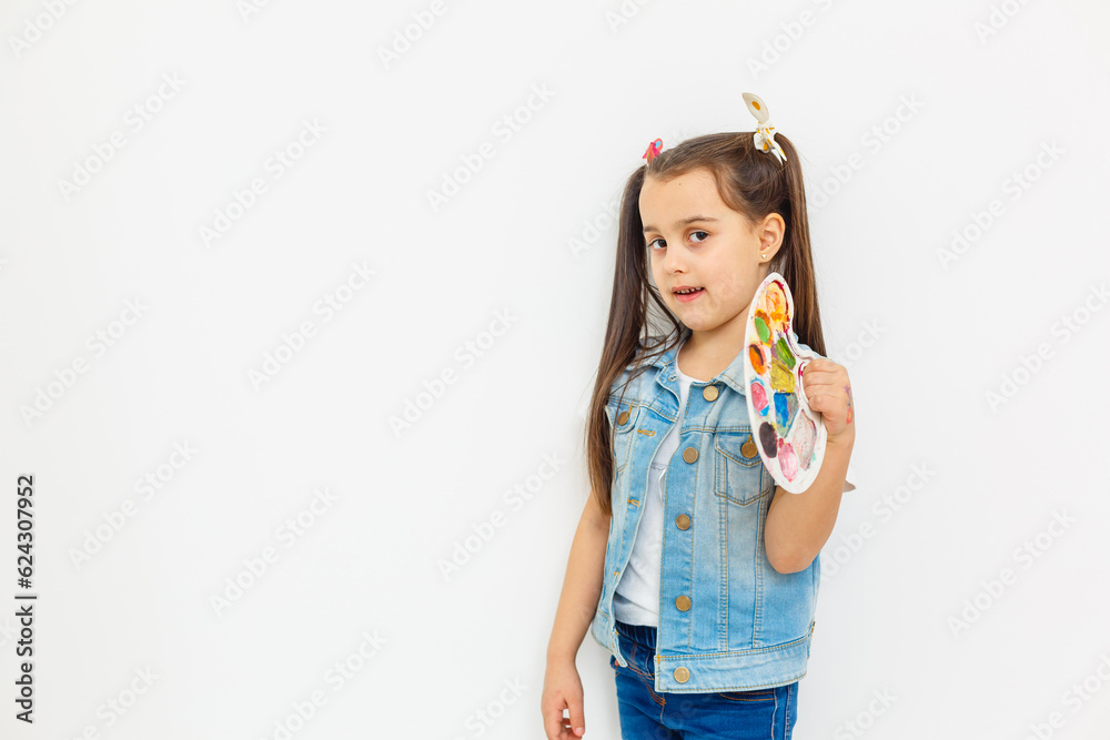 A joyful little girl with a paint palette and a brush on a white background. A joyful little girl with a paint palette and a brush on a white background.