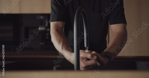 A man washes his hands at home in the modern kitchen interior. Contemporary modern and minimalist design apartment, Stylish interior of the luxury kitchen with italian design. Modern black faucet.
