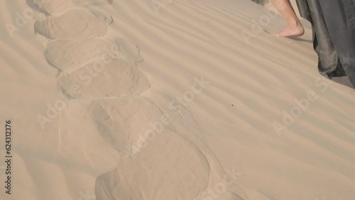 Young woman with long hair in an elegant black dress walking barefoot on the sand dunes of the desert photo