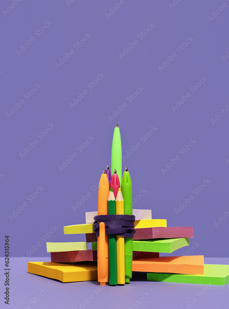 Stationery rocket out of pens on desk on top of pile of sticky notes. purple background. back to school or education and creativity concept. Success achievement. Team work ideas and leadership Stationery rocket out of pens on desk on top of pile of sticky notes. purple background. back to school or education and creativity concept. Success achievement. Team work ideas and leadership