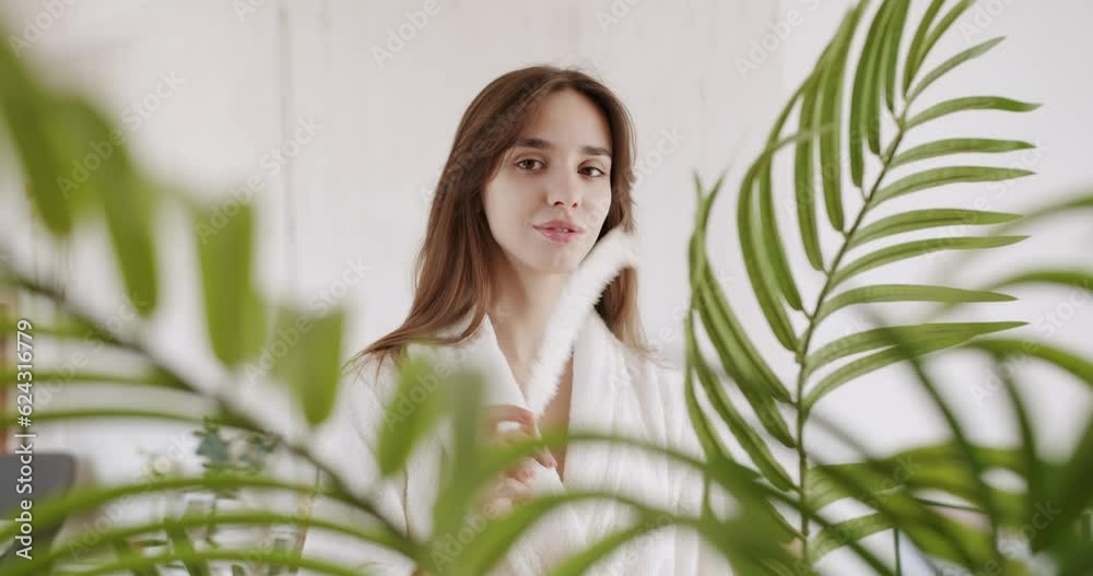 Portrait of young beautiful woman with nude makeup holding playing with feather on face. Beautiful woman enjoying smooth skin condition at home and smiling, slow motion. Skin care concept at home. Portrait of young beautiful woman with nude makeup holding playing with feather on face. Beautiful woman enjoying smooth skin condition at home and smiling, slow motion. Skin care concept at home.