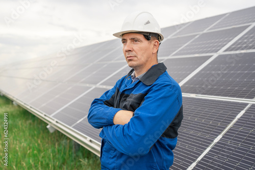 Service Engineer man standing with arms crossed in front of solar panels. Technician maintenance solar cells on Solar Energy Plant under morning sunlight. Technology solar energy renewable