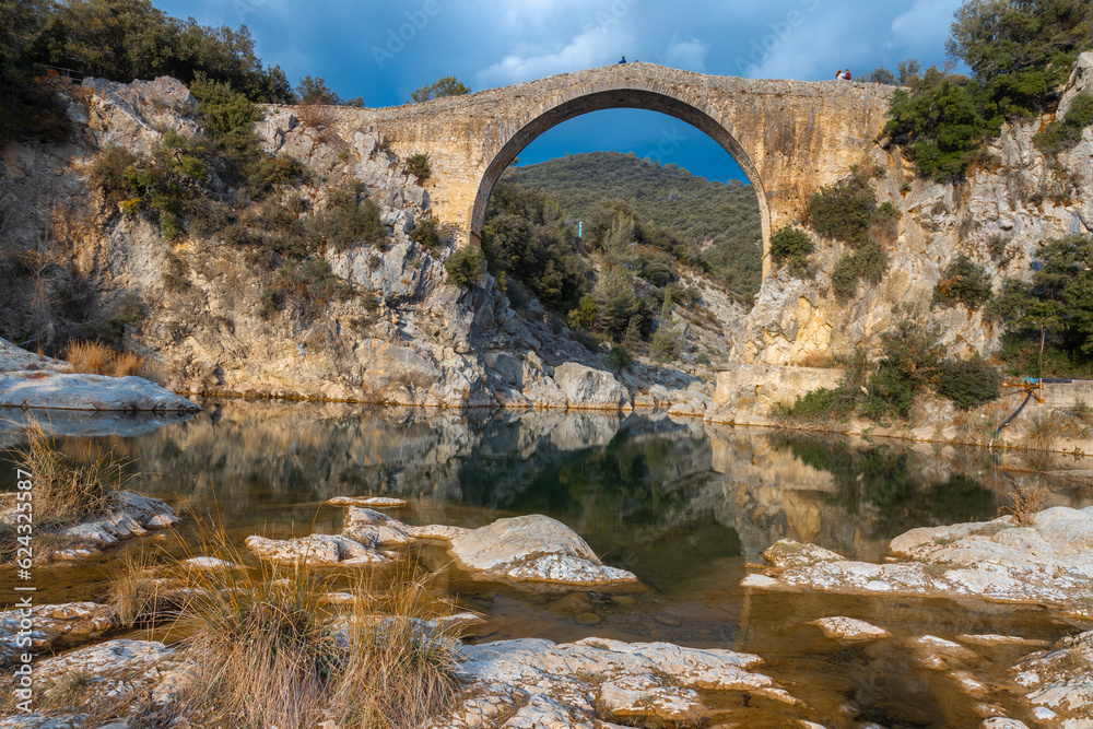 View of an ancient bridge Pont de Llierca in Catalonia, Spain. This beautiful bridge, paved with sandstone slabs, is in use since the 14th century.