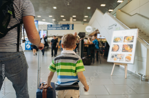 Father and cute caucasian boy in airport with backpack and suitcase. Travelling with kids