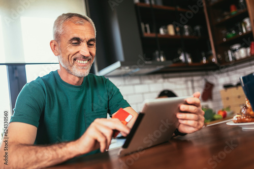 Mature man in kitchen using digital tablet for online payment
