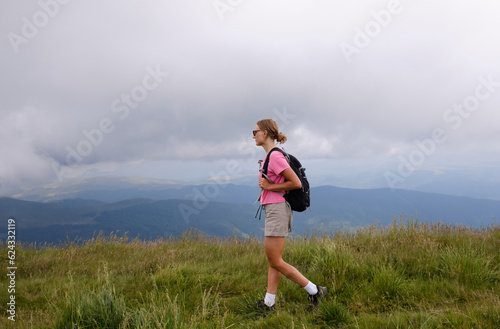 Woman is hiking in mountains in summer.Beautiful mountain landscape in Carpathians, Romania.Travel and tourism.Woman hiker is enjoying the mountain view.