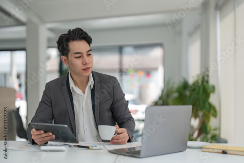 Focused young adult businessman asian sitting at desk making sure his company is earning enough money financial planning concept