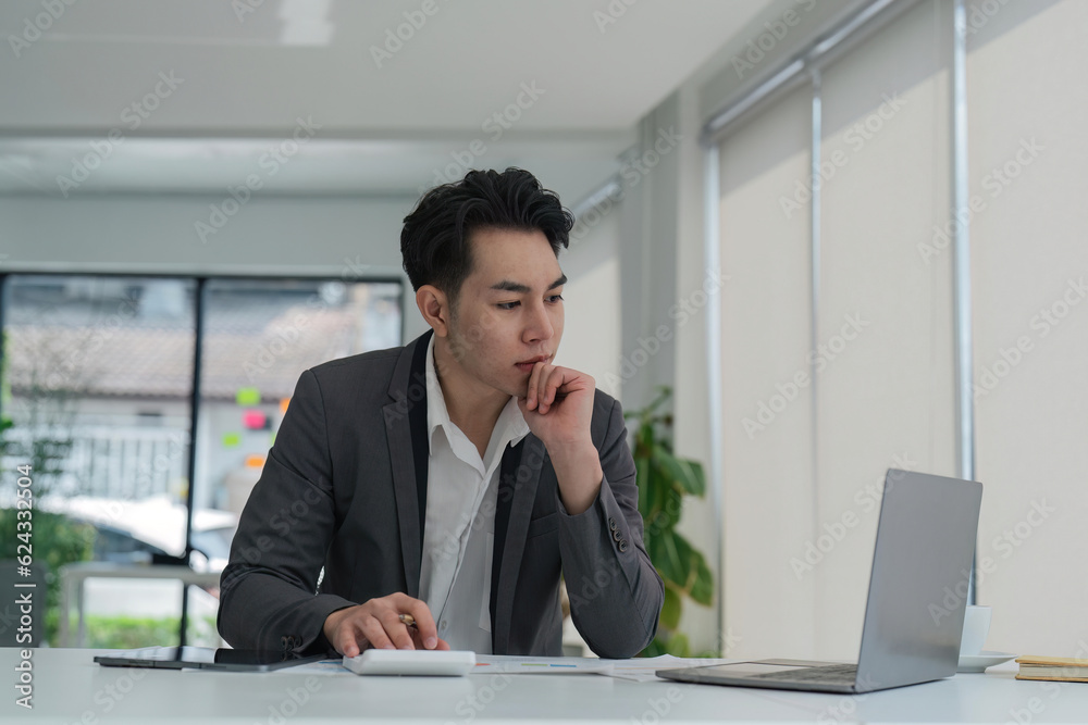 Focused young adult businessman asian sitting at desk making sure his company is earning enough money financial planning concept Focused young adult businessman asian sitting at desk making sure his company is earning enough money financial planning concept