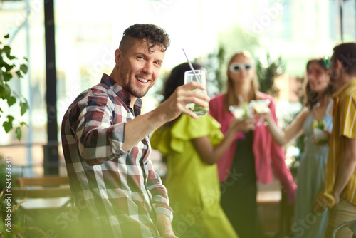 Photography Focus on smiling man raising glass with cocktail, attending party with friends at cafe